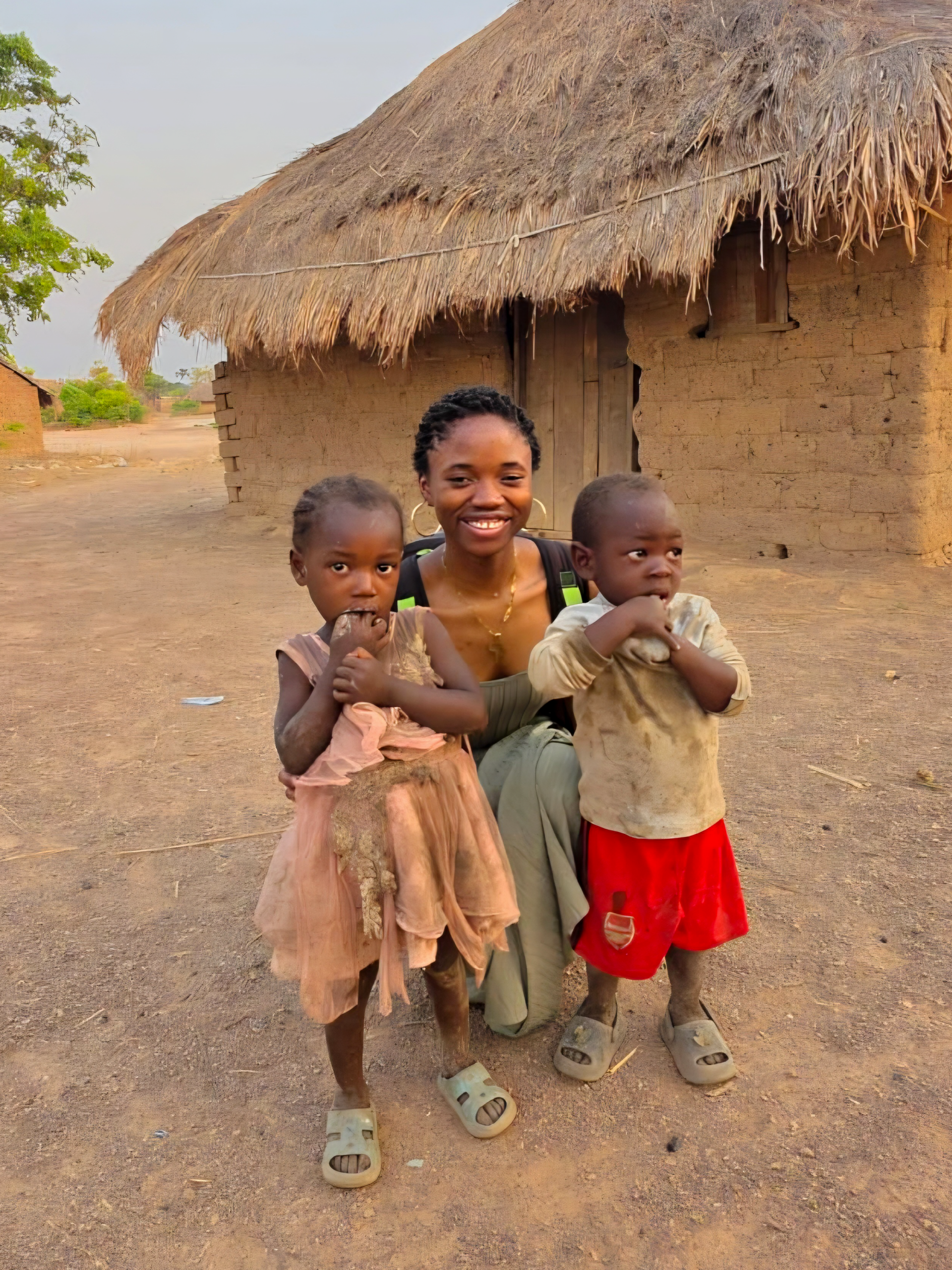 Ntumba with two young children outside a thatched home in the Democratic Republic of Congo